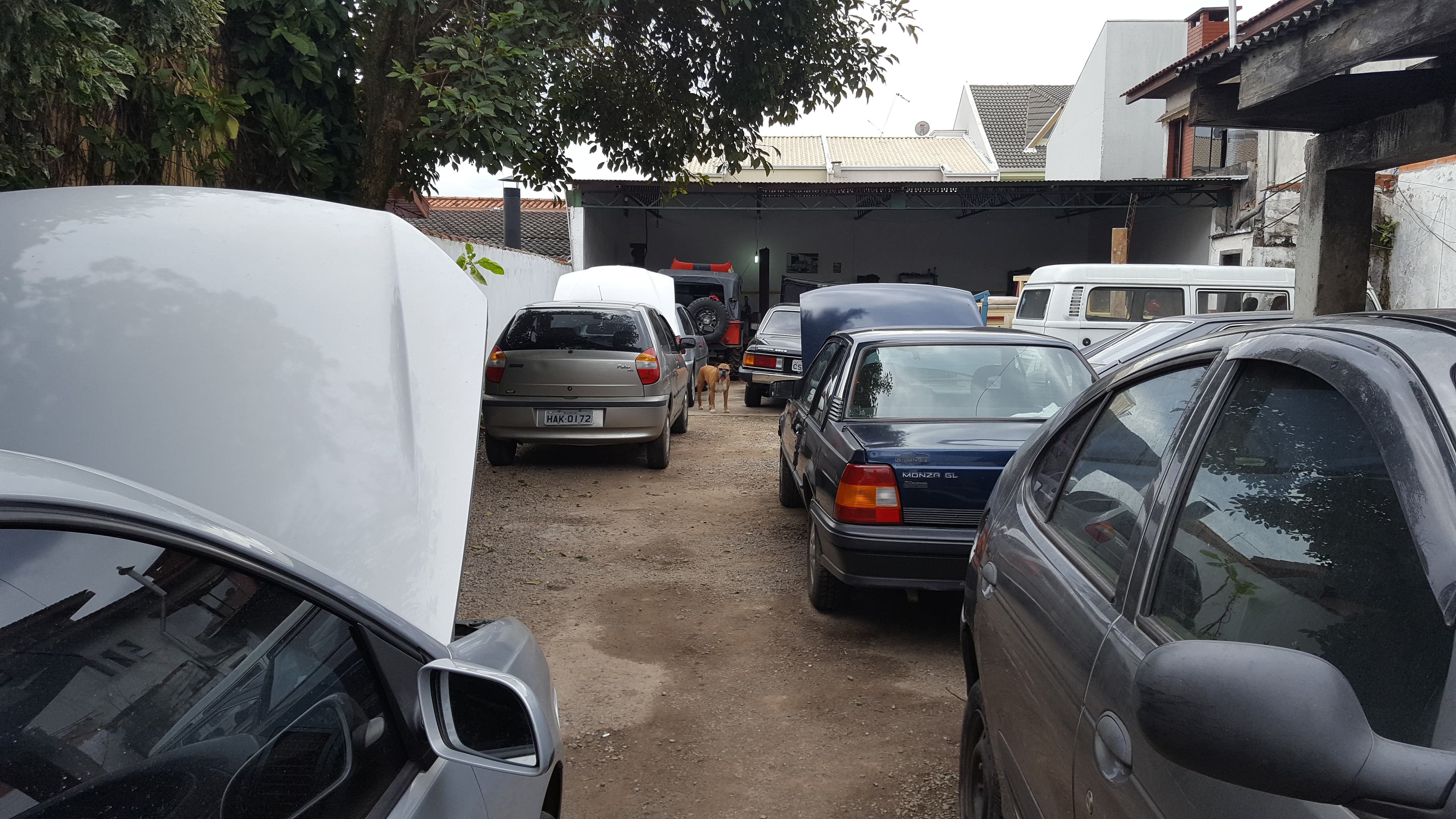 Pátio da oficina com Kombi, Monza e Jeep de capô aberto