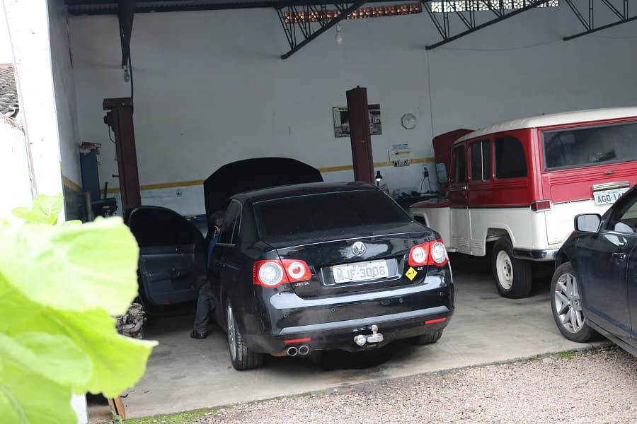 Rural Willys vermelha e branca dentro da oficina, ao lado de um sedã moderno