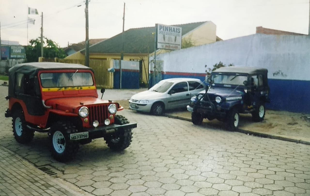 Dois Jeeps Willys restaurados, um vermelho e um azul, na porta da Pinhais Carburadores